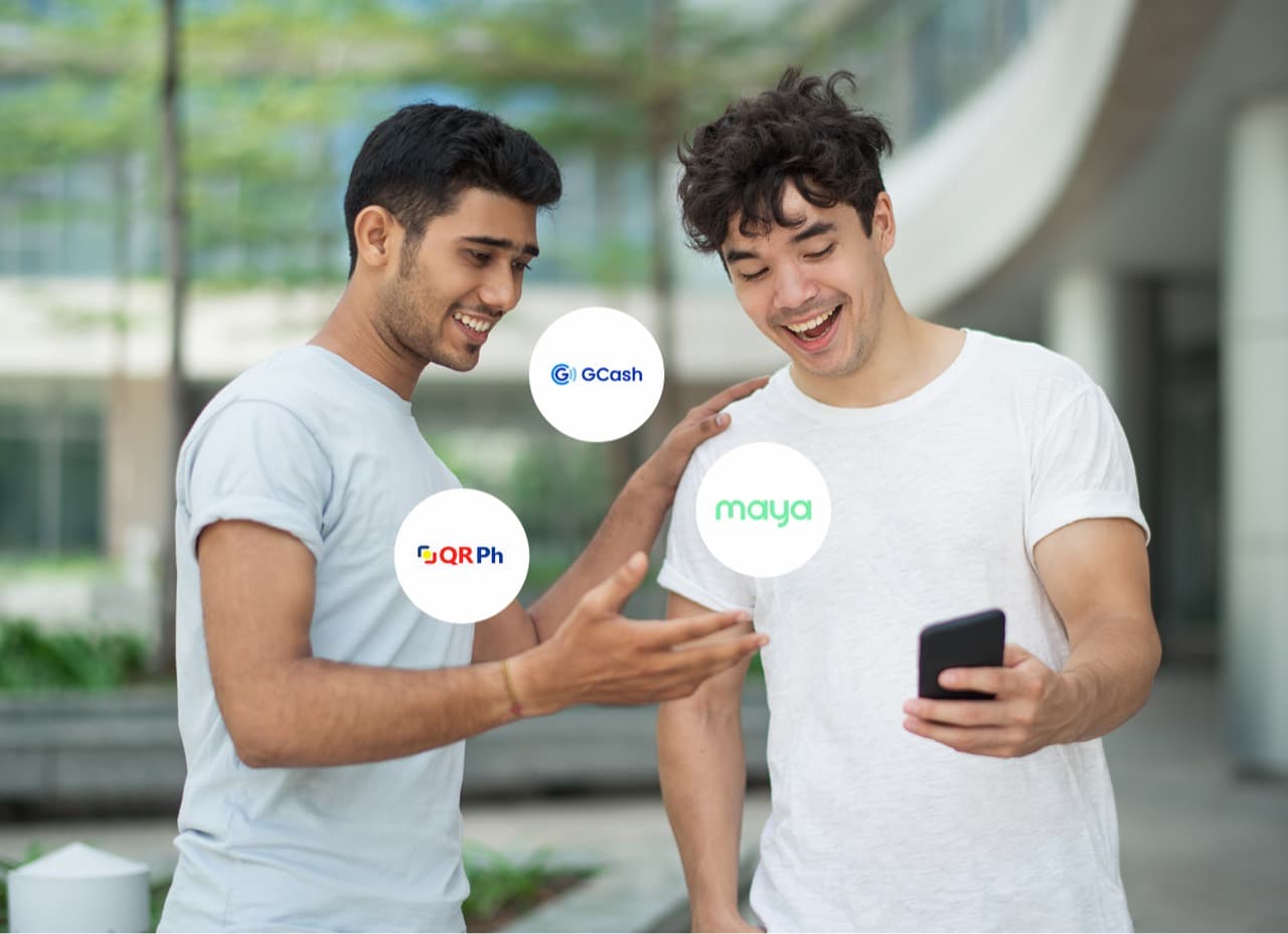 Two friends smiling at a phone, ringed by GCash, Maya, and QR Ph payment badges